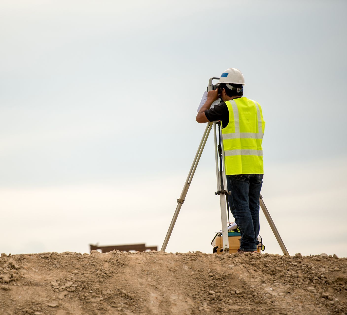 Un homme portant un gilet jaune se tient au sommet d'une colline de terre et regarde à travers un télescope.