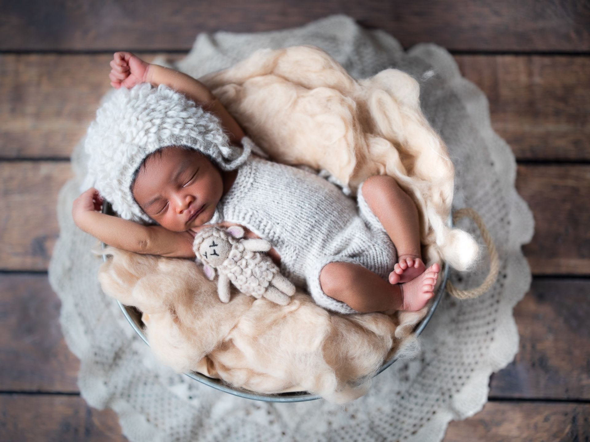 A newborn baby is sleeping in a bucket with a stuffed animal.