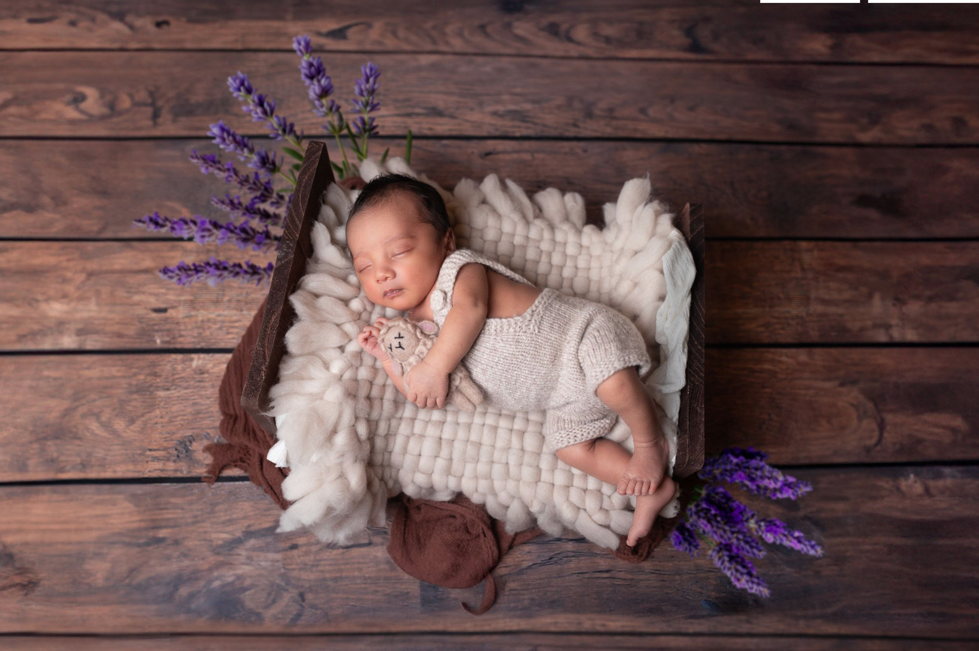 A newborn baby is sleeping in a basket on a wooden floor.