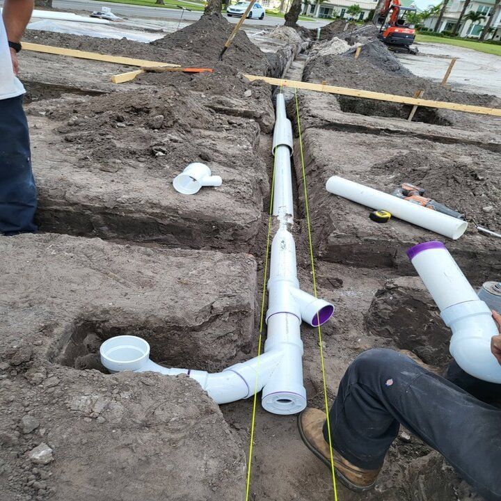 A plumber in blue shirt uses a wrench on sink pipes in a white-tiled bathroom.
