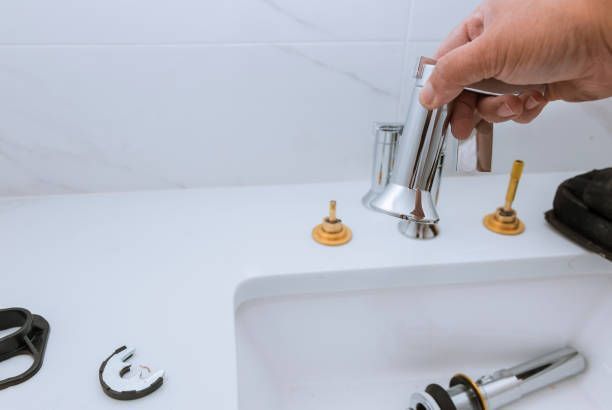 A person replacing a faucet in a white sink with tools and parts.