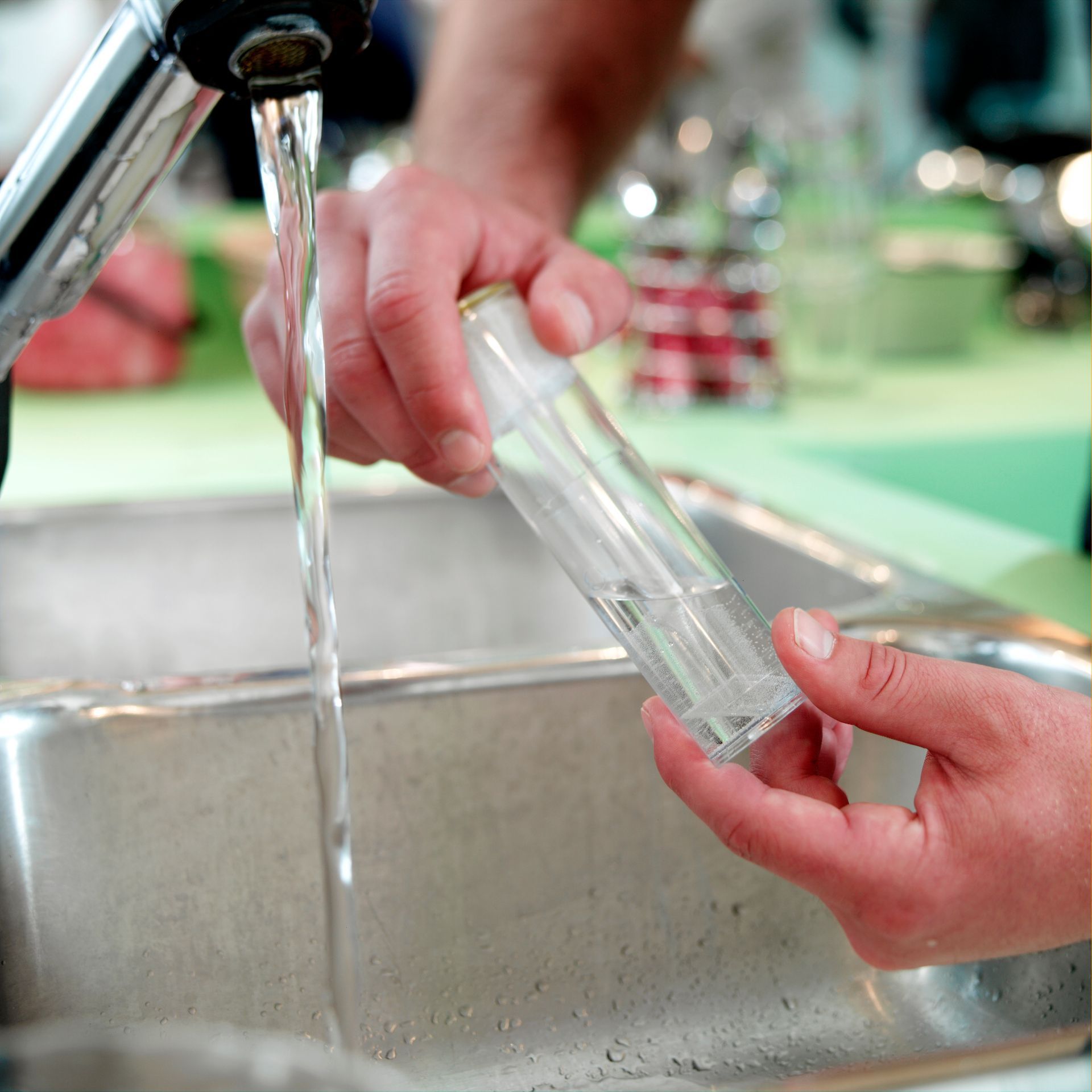 Person filling a glass vial with water at a sink, lab setting.