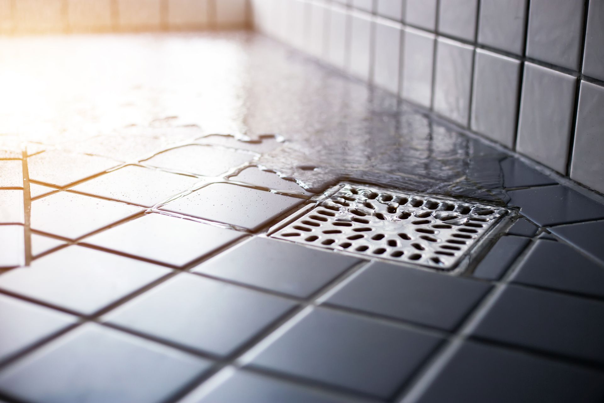 Close-up of a tiled shower floor with water pooling around a square drain.