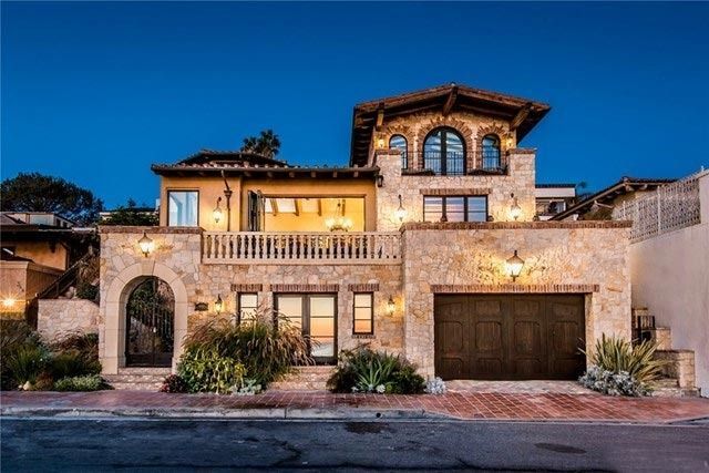 Luxury stone house at dusk with warm-lit windows, arched entryway, balcony, and two-car garage
