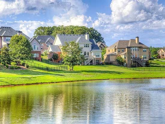 Quiet suburban lakeside homes with green lawns reflected in calm water under a blue sky