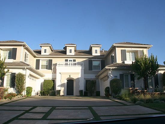 Large white mansion with a symmetrical facade, arched entryway, and a wide driveway under a clear blue sky