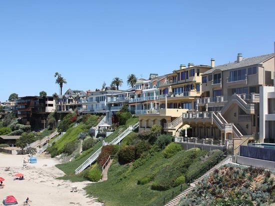 Beachfront condos overlooking a sandy beach with stairs and greenery under a clear blue sky