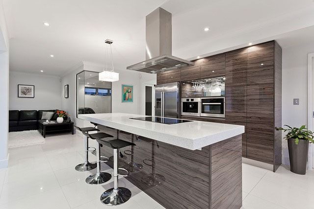 Modern open kitchen with white island, bar stools, stainless appliances, and gray wood cabinetry