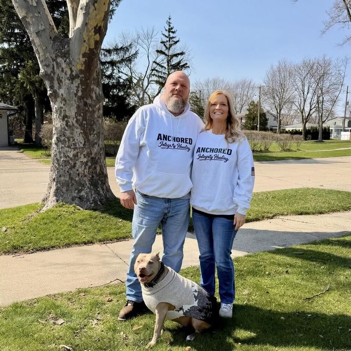 A navy blue anchor wrapped in a tan rope, centered on a shield displaying the American flag pattern.