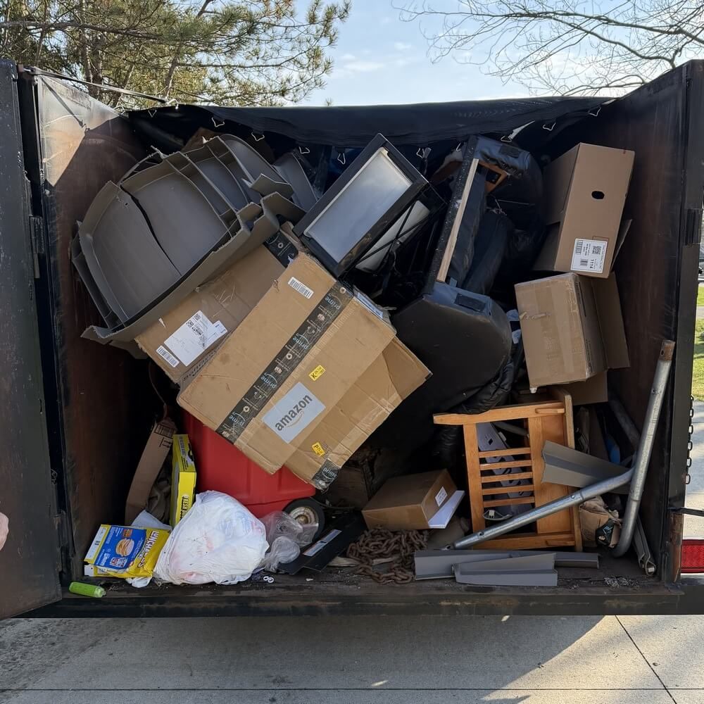 A black and white graphic of a junk removal trailer filled with discarded furniture and a bag.