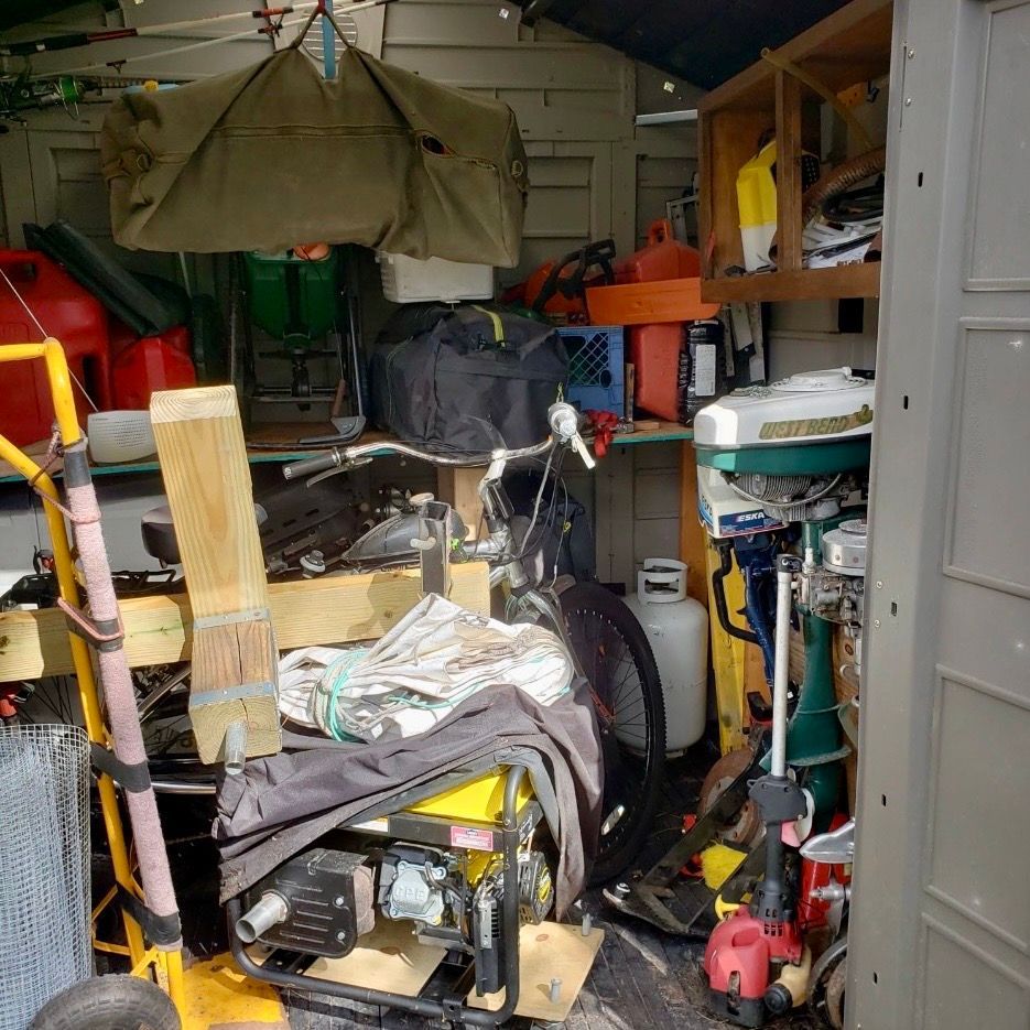 A room filled with various household items, packed boxes, plastic containers, and clutter stacked floor to ceiling.