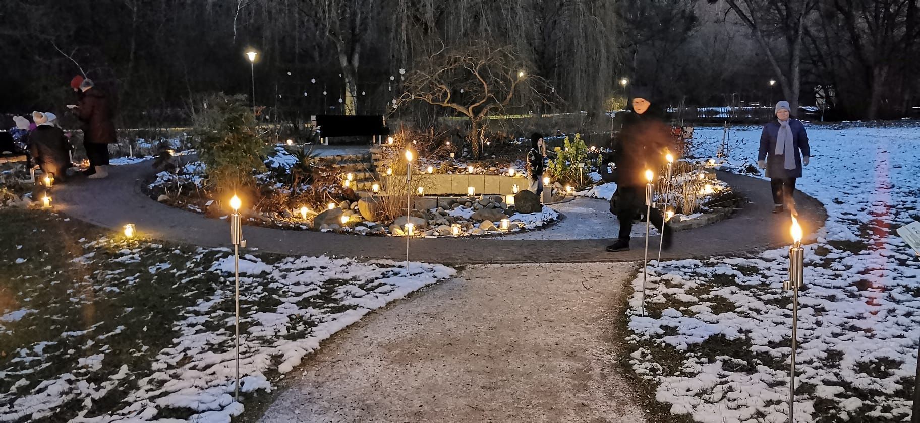 Menschen mit Fackeln gehen nachts auf einem schneebedeckten, beleuchteten Pfad.