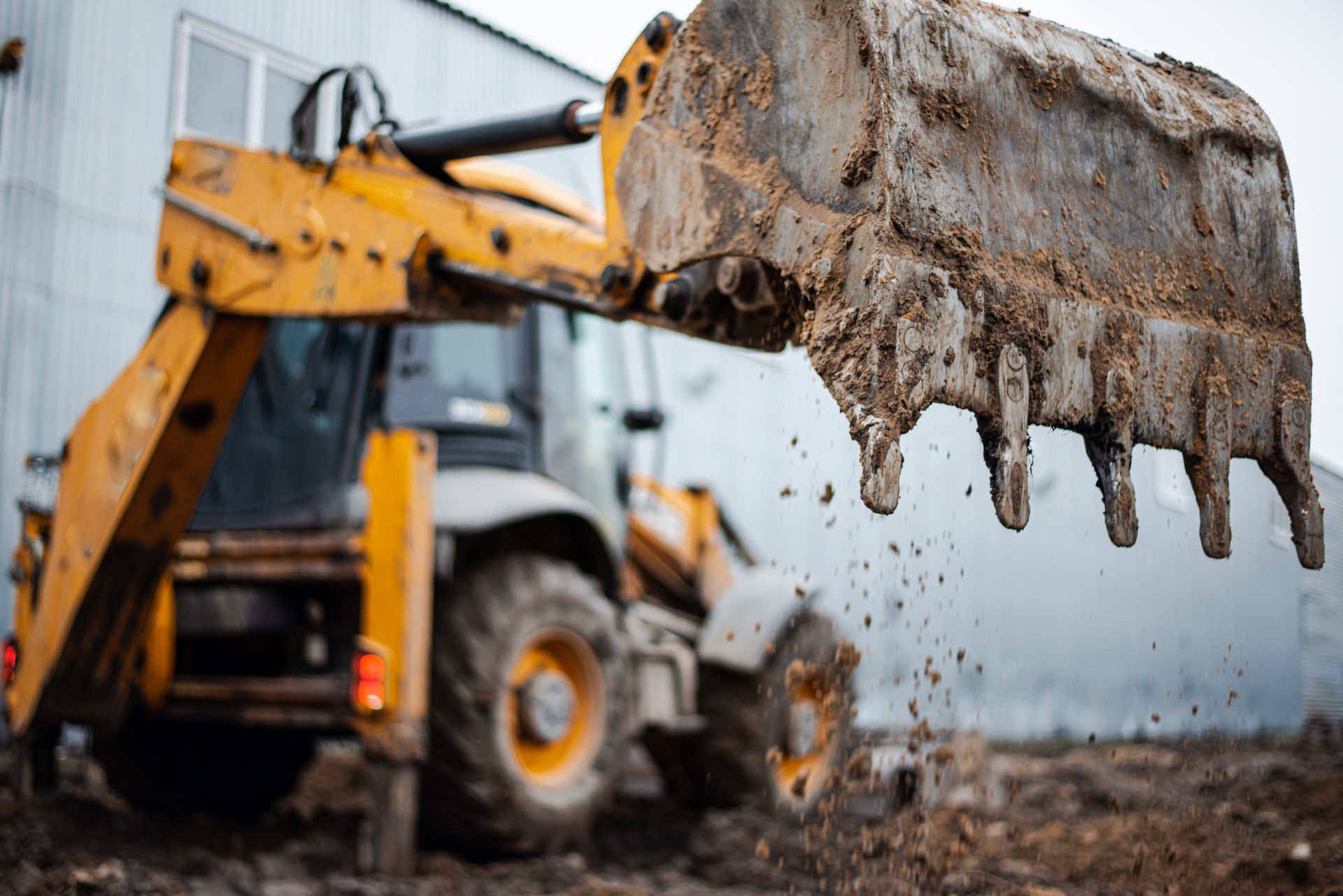 Mud-covered excavator bucket dripping soil at a construction site.