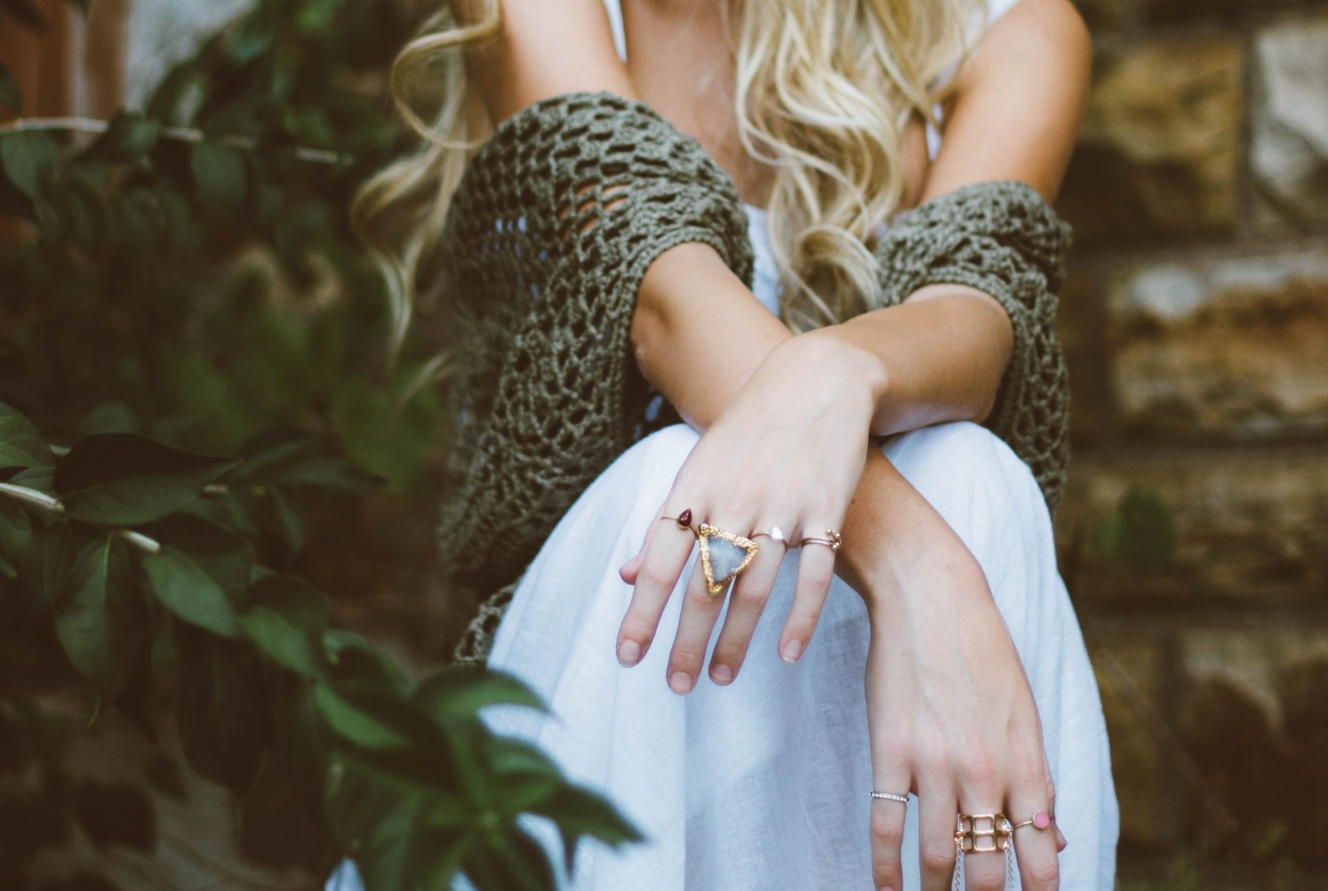 A woman in a white dress is sitting on a staircase with her arms crossed and wearing rings on her fingers.