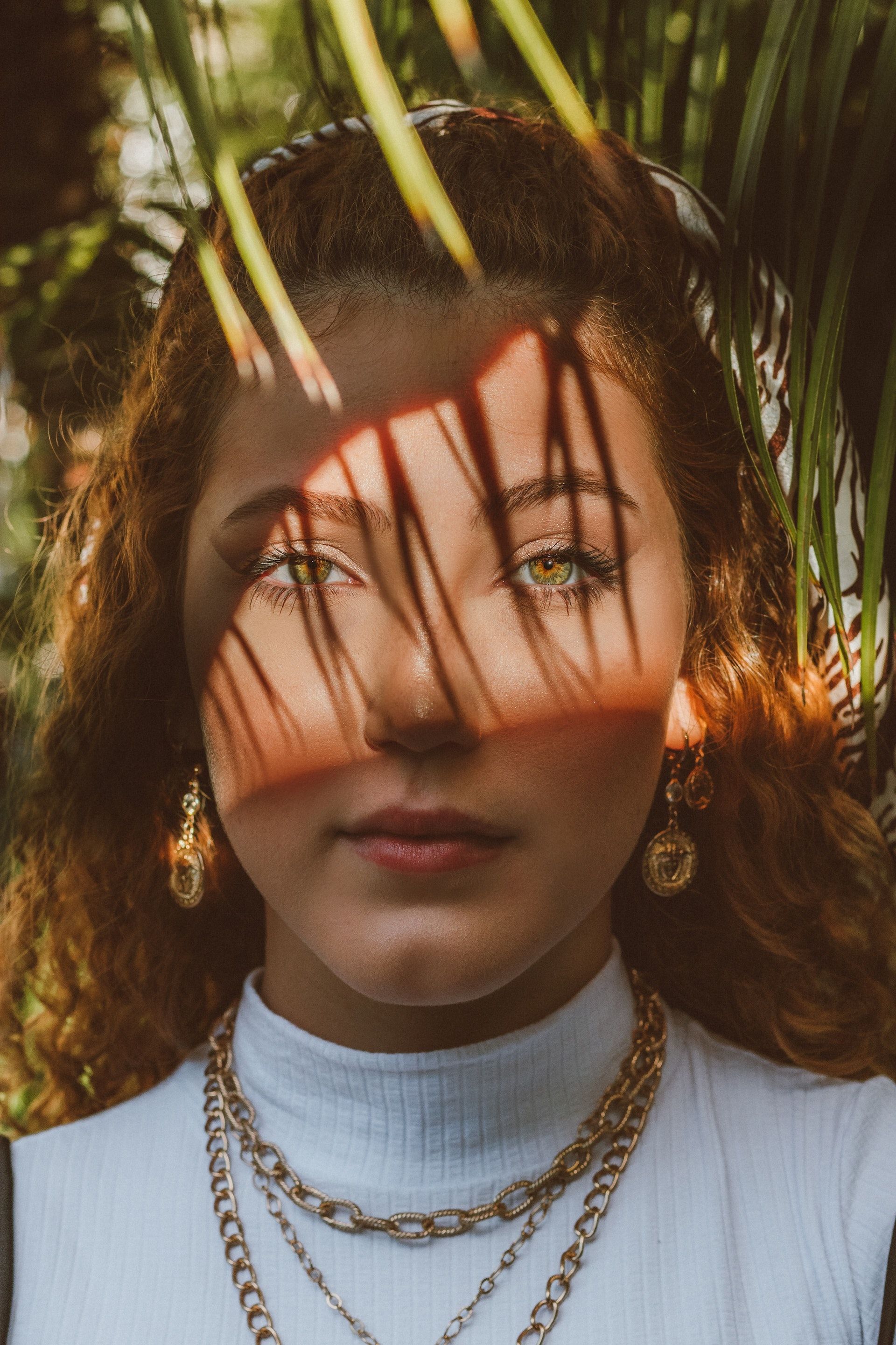 A woman wearing a necklace and earrings is standing in front of a palm tree.