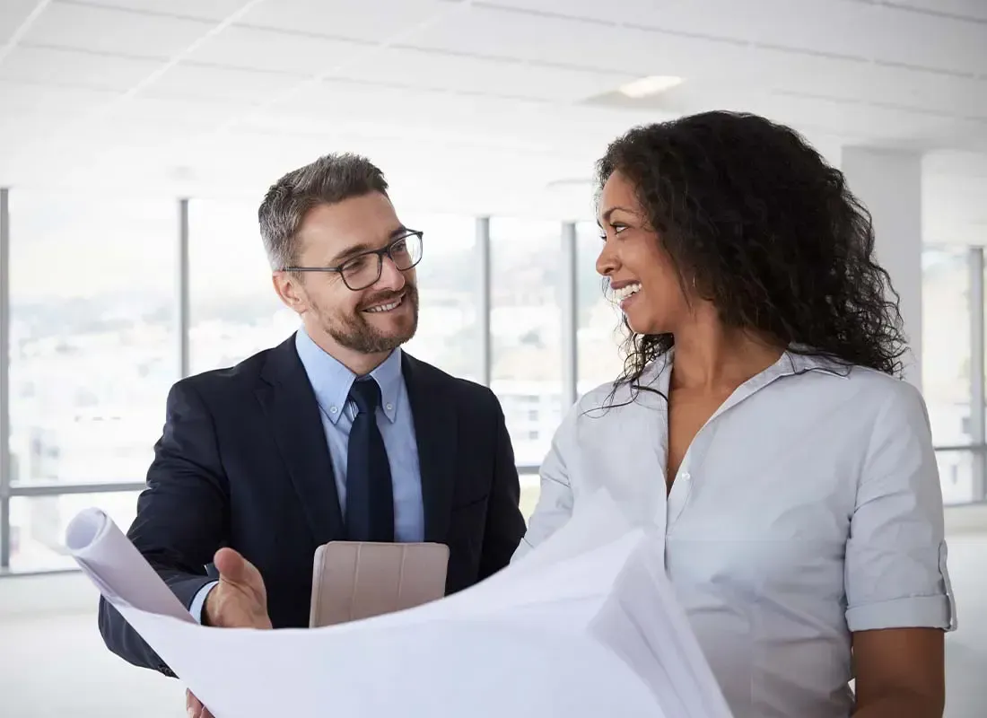 A professional in a suit and a professional in a light shirt discuss building plans inside a bright, modern office space.