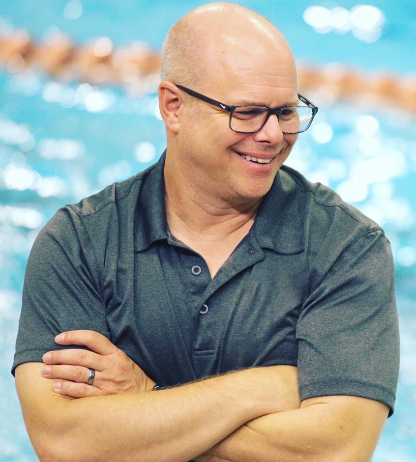 A woman in an orange shirt is smiling and wearing a necklace.