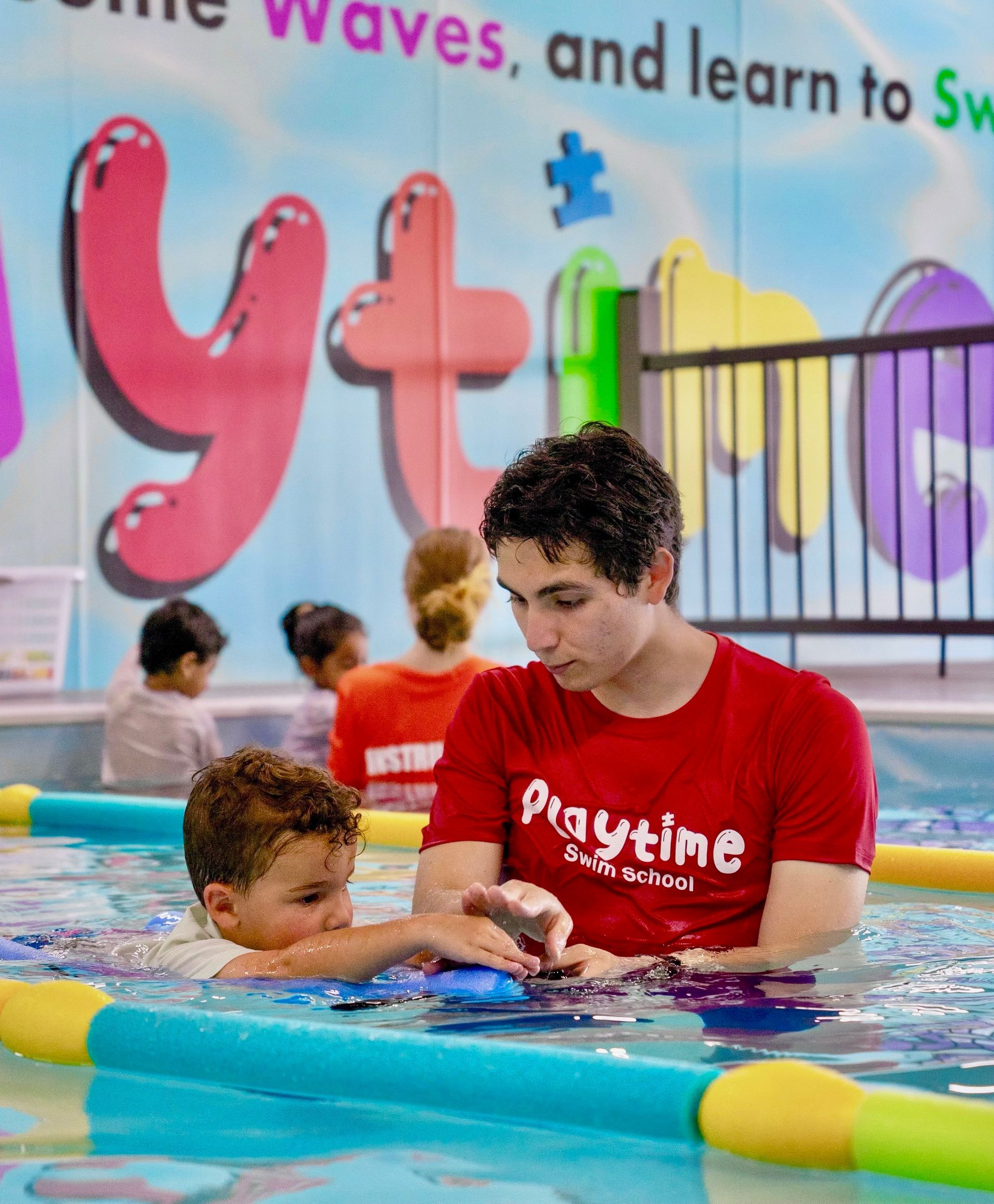 A man in a red playtime shirt is playing with a child in a pool
