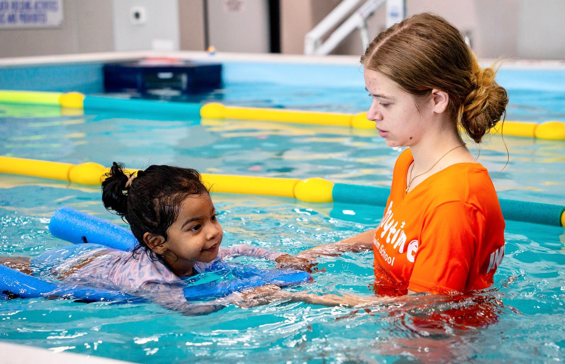 A woman is teaching a little girl how to swim in a swimming pool.