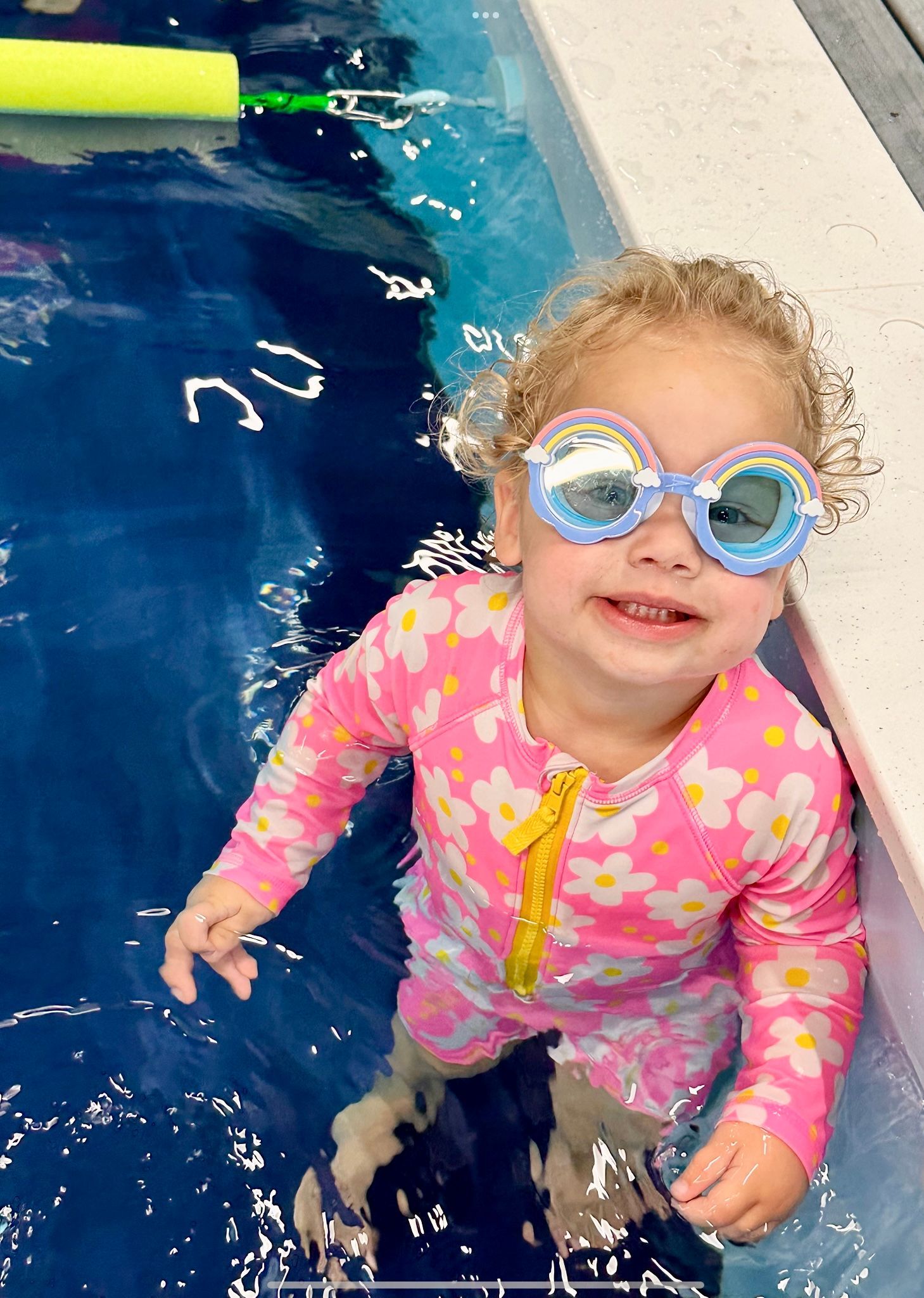 A little girl wearing goggles is standing in a swimming pool.