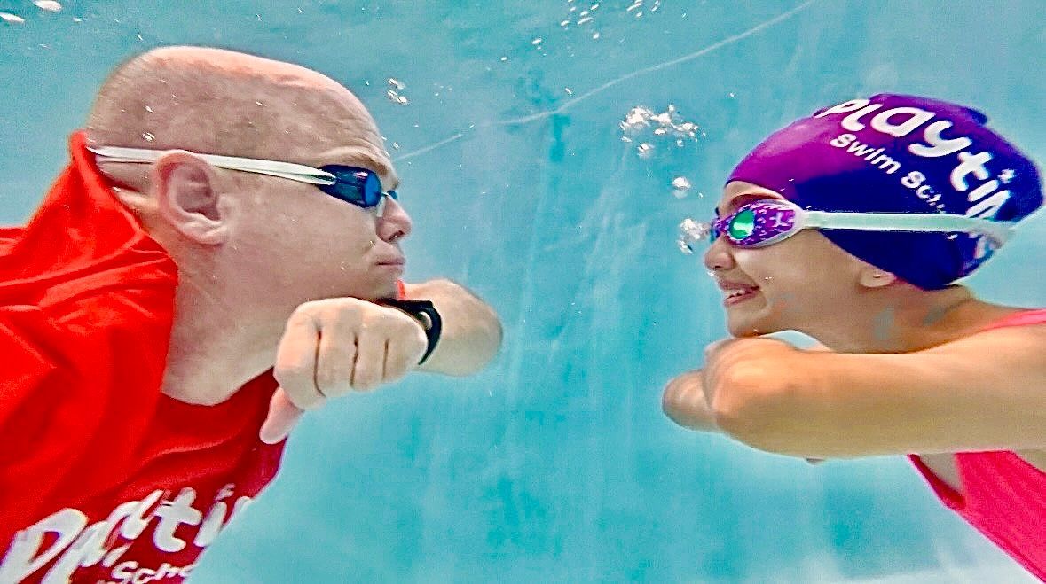 A man and a girl are swimming underwater in a pool.