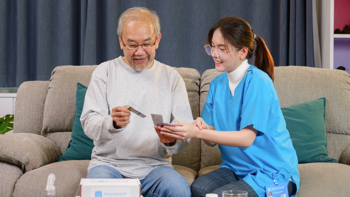 An elderly man is sitting on a couch with a nurse.