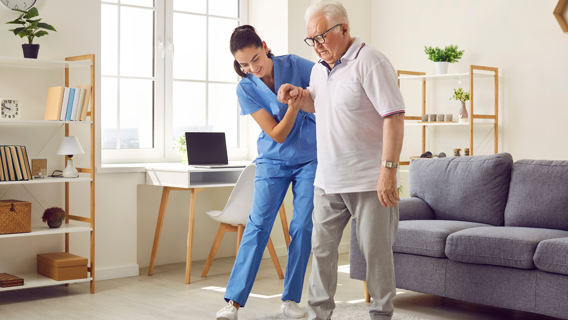 A nurse is holding the hand of an elderly woman who is sitting on a couch.