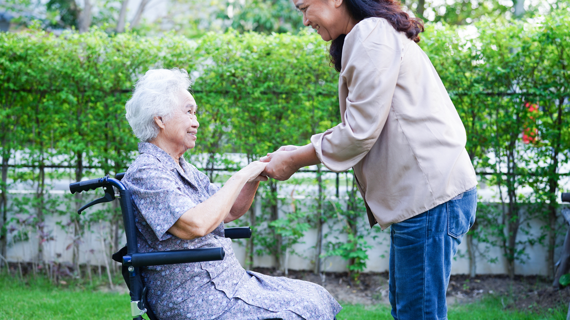 A woman is holding the hand of an elderly woman in a wheelchair.