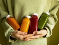 Person holding four colorful juice bottles.