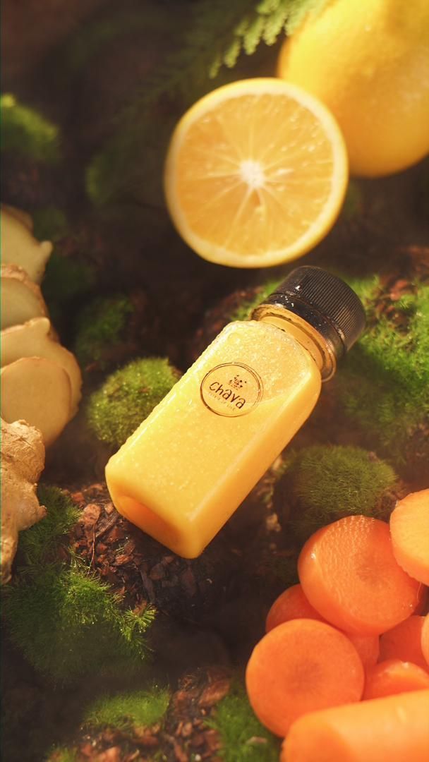 Bottle of yellow juice with lemon, carrot, and ginger on moss.