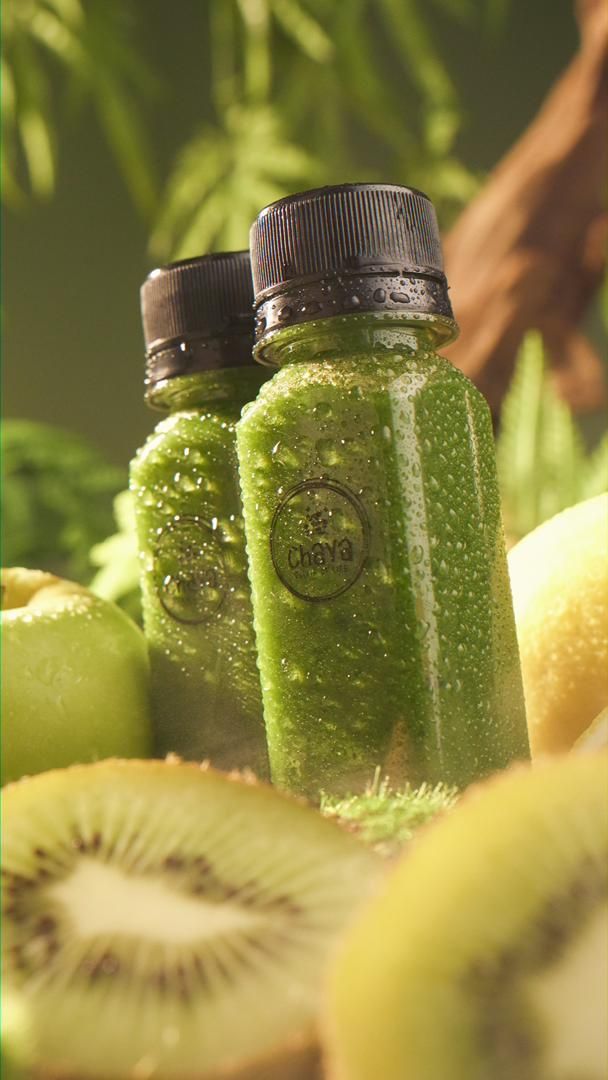 Two small green juice bottles surrounded by kiwi, apple, and lemon slices.