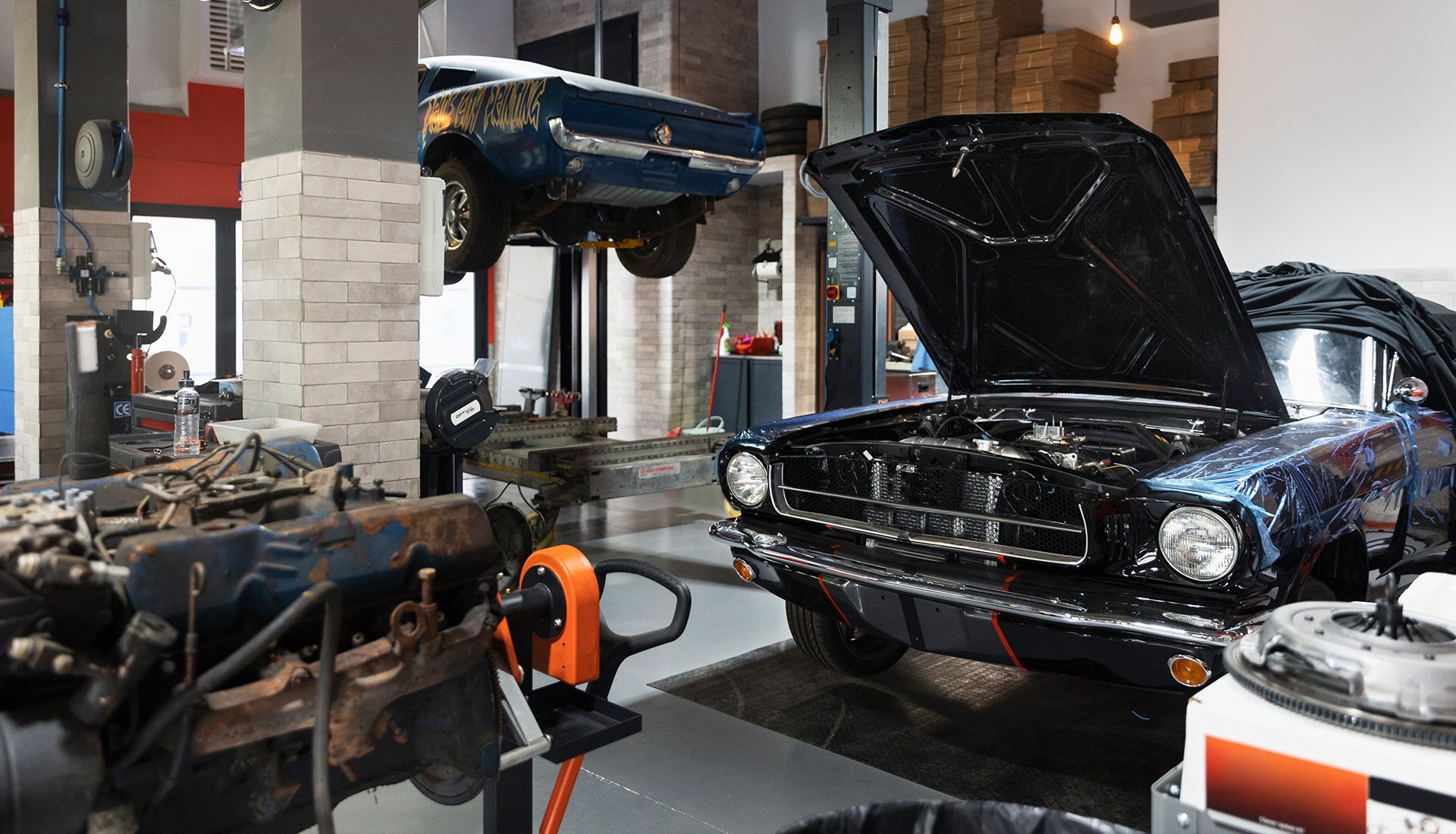 Classic cars in an auto shop, one raised on a lift, another with its hood open.
