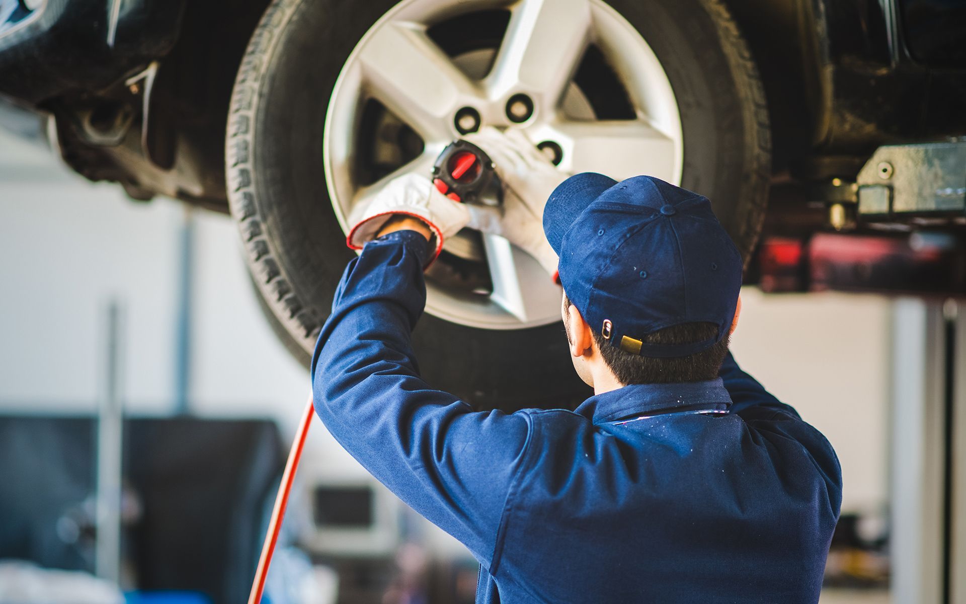Mechanic using an impact wrench on a car tire in a garage.