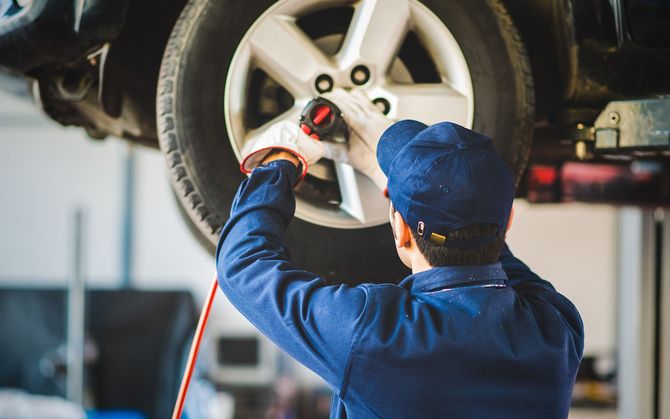 Mechanic using an impact wrench on a car tire in a garage.