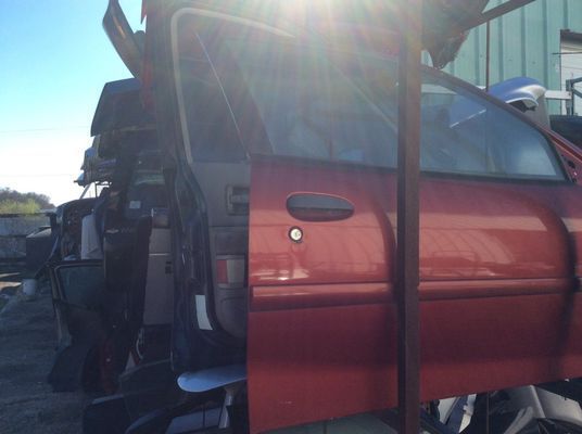 Red car door in a junkyard, open. Sunlight shines.