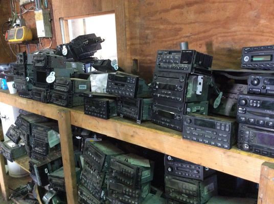 Shelves filled with piles of car radios in a cluttered workshop.