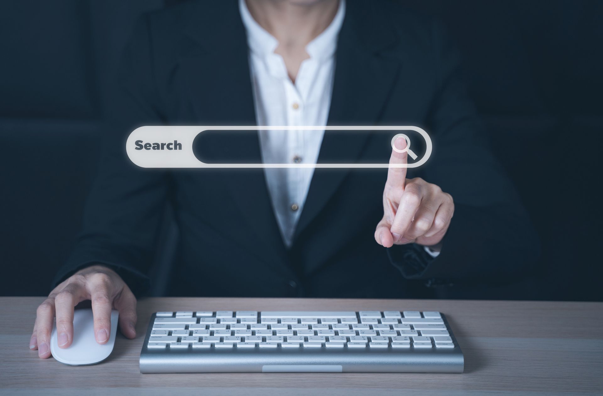 Person in a suit interacting with a virtual search bar above a keyboard and mouse.
