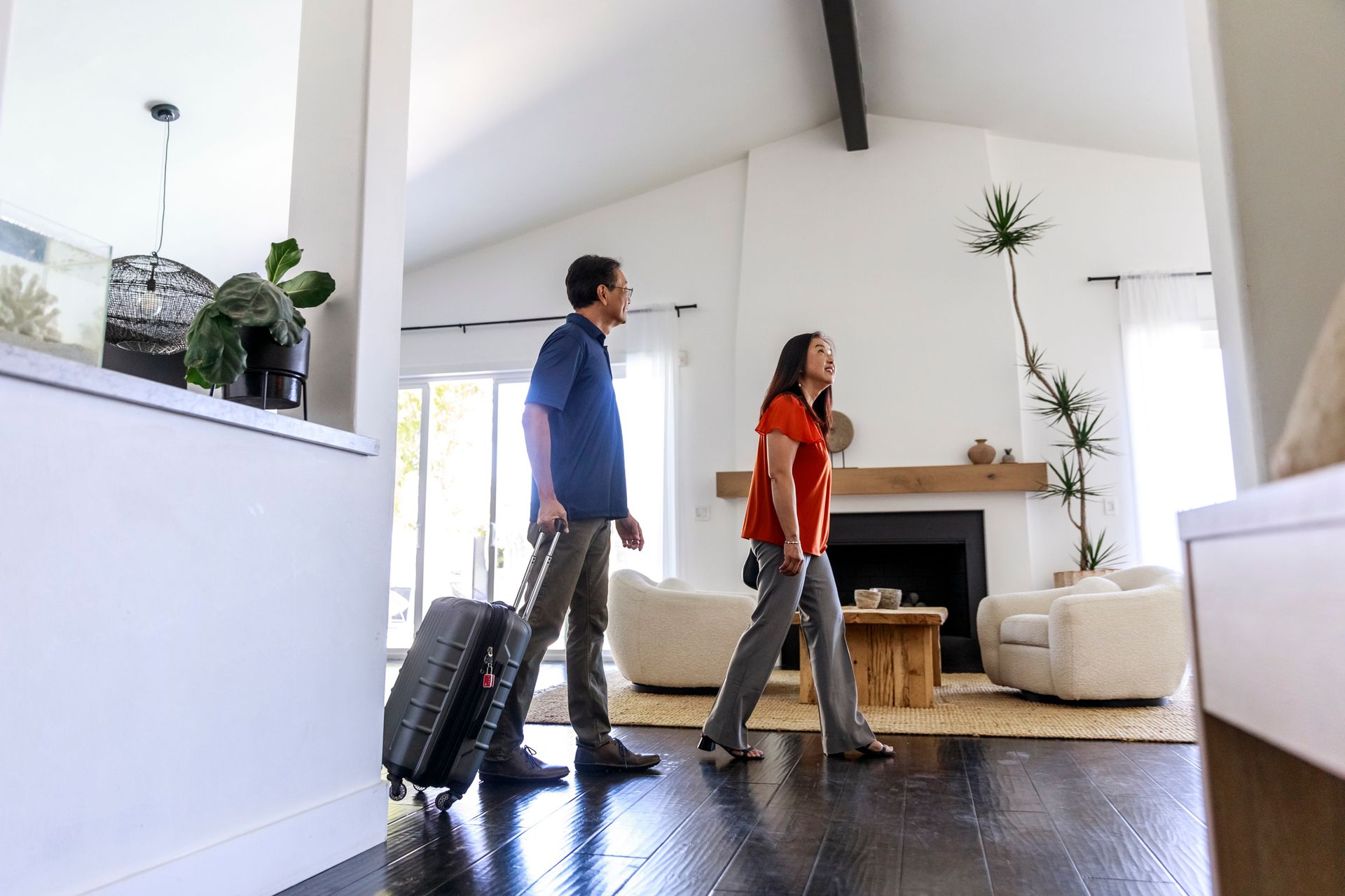 Couple walking through a bright modern home, one rolling a suitcase.