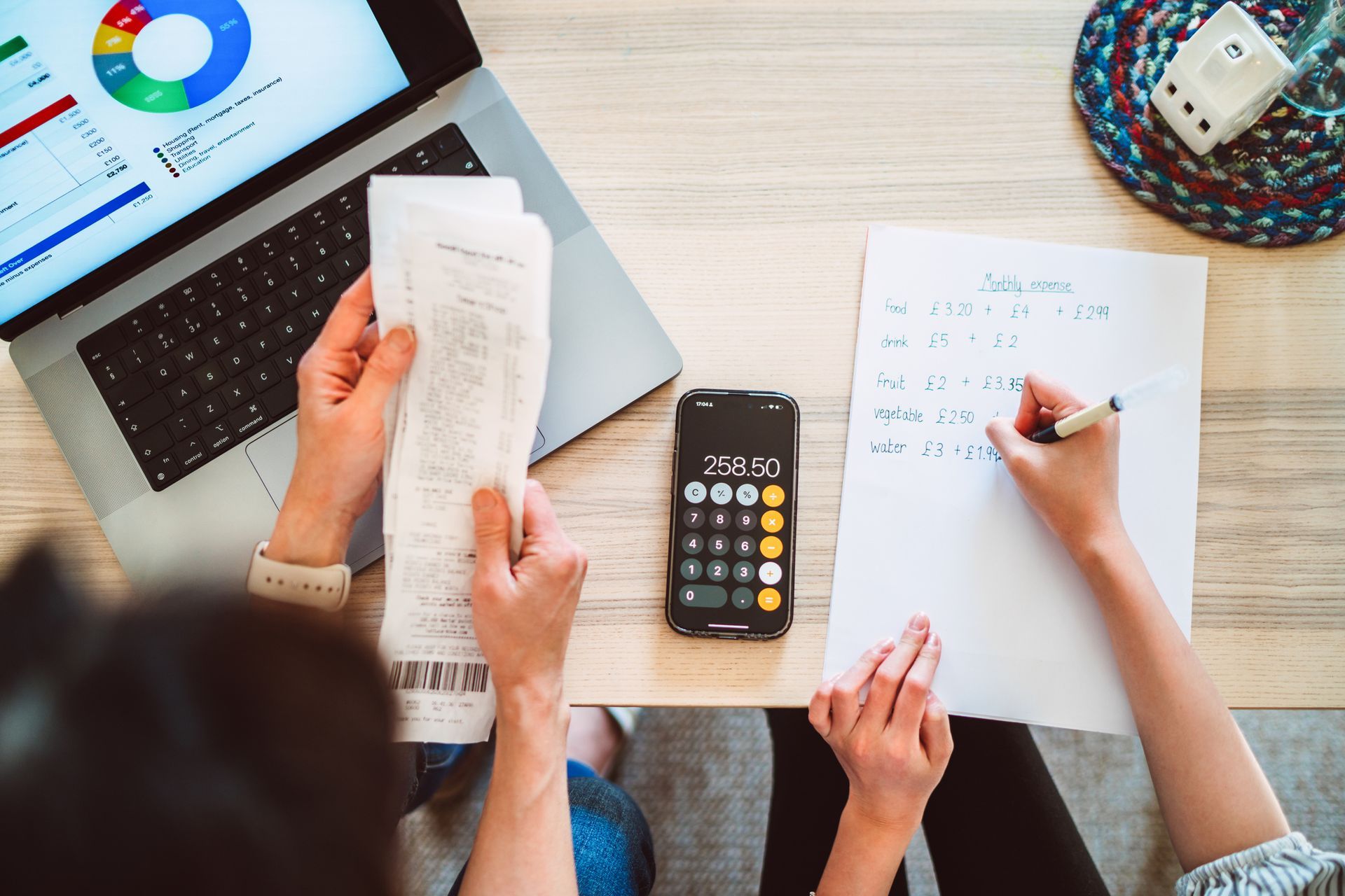 Person reviewing receipts and calculating expenses using calculator, laptop, and paper on a table.