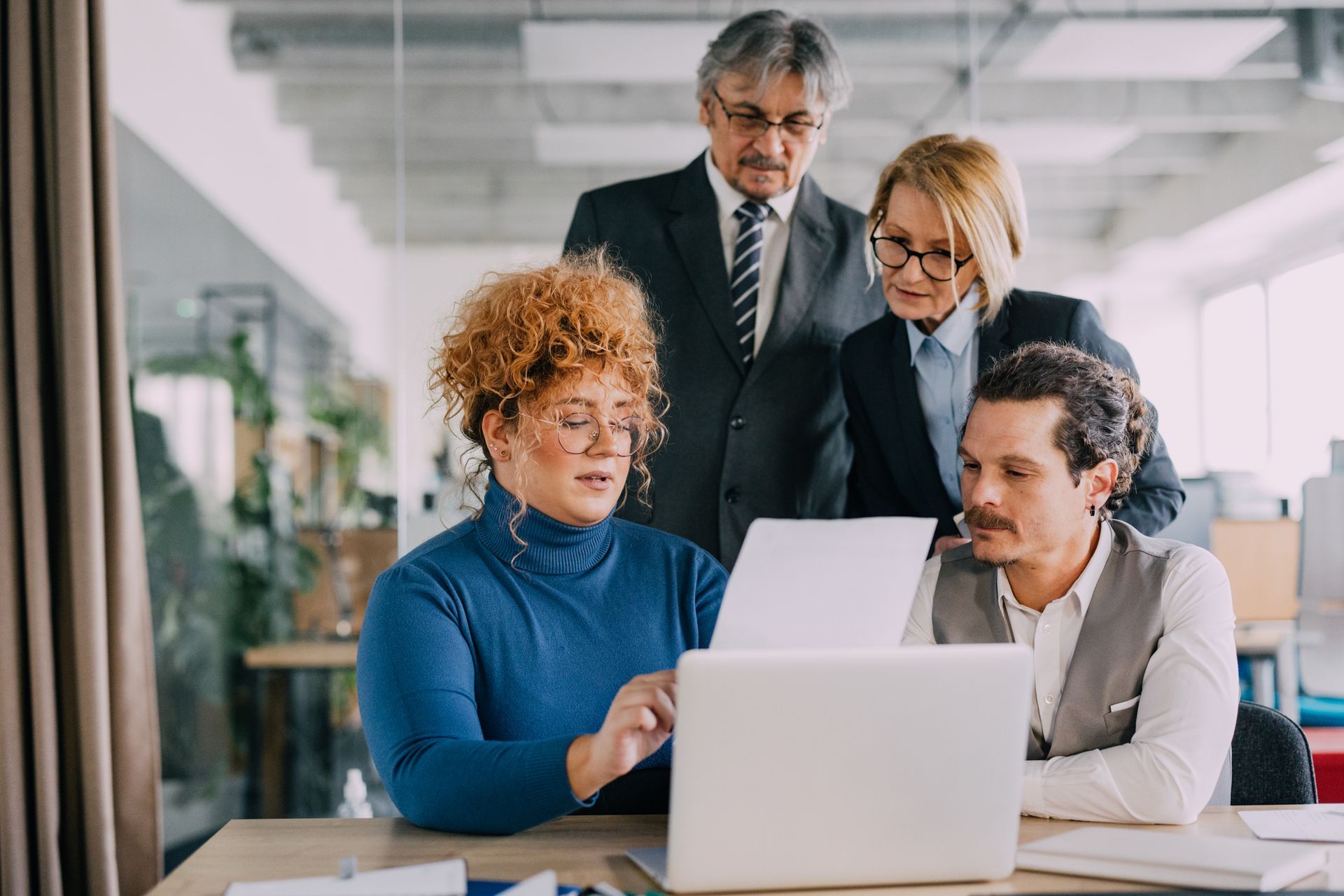 Four business people looking at laptop and paperwork in office.
