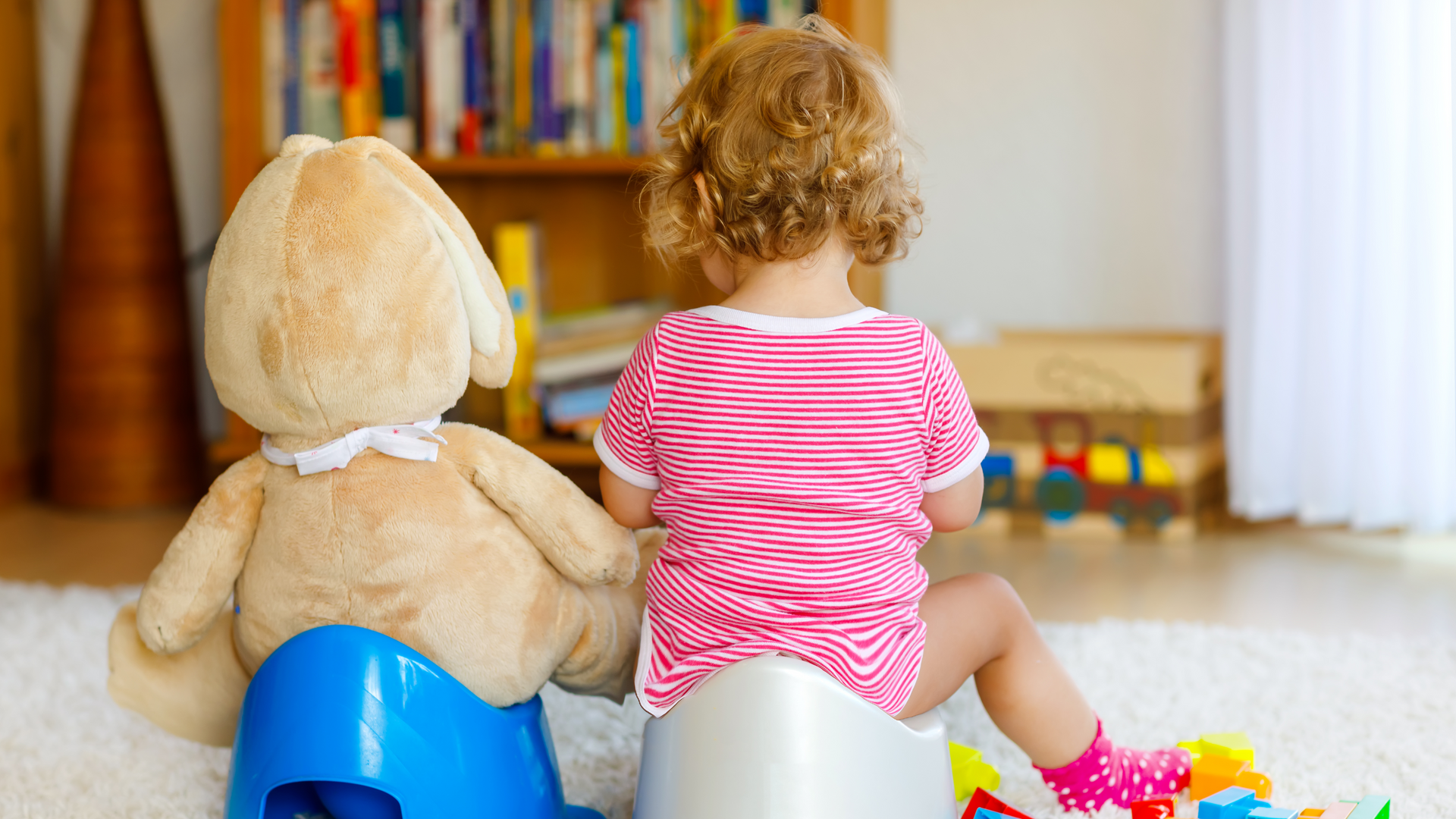 A little girl is sitting on a blue potty next to a teddy bear.
