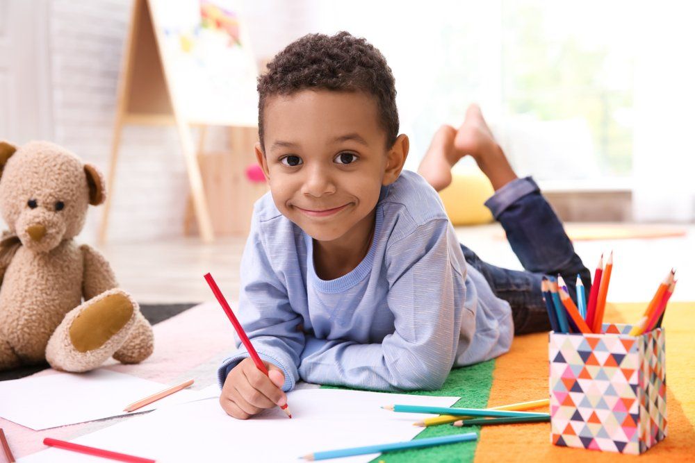 A young boy is laying on the floor drawing with colored pencils.