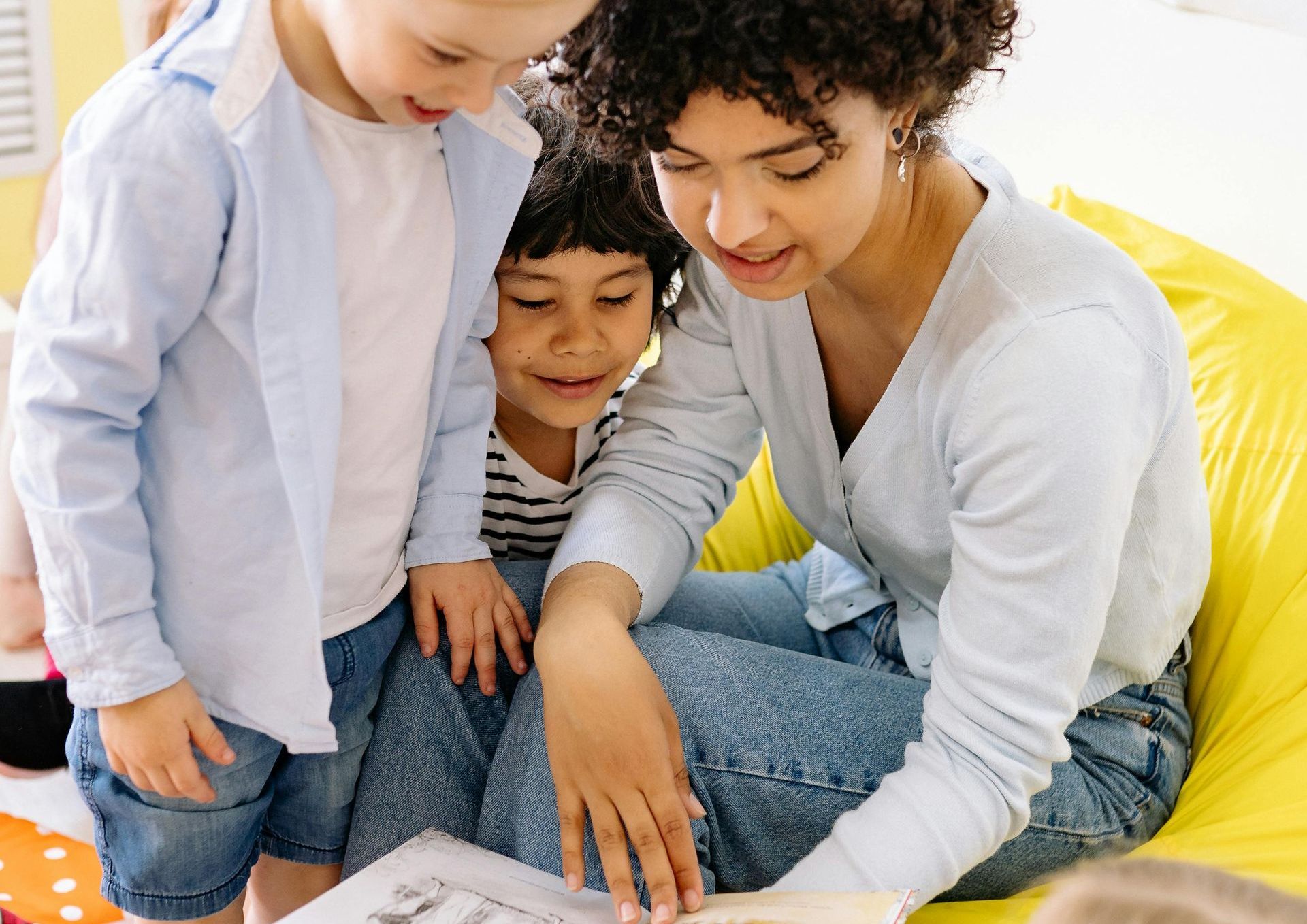 A woman is sitting on a bean bag chair reading a book to two children.