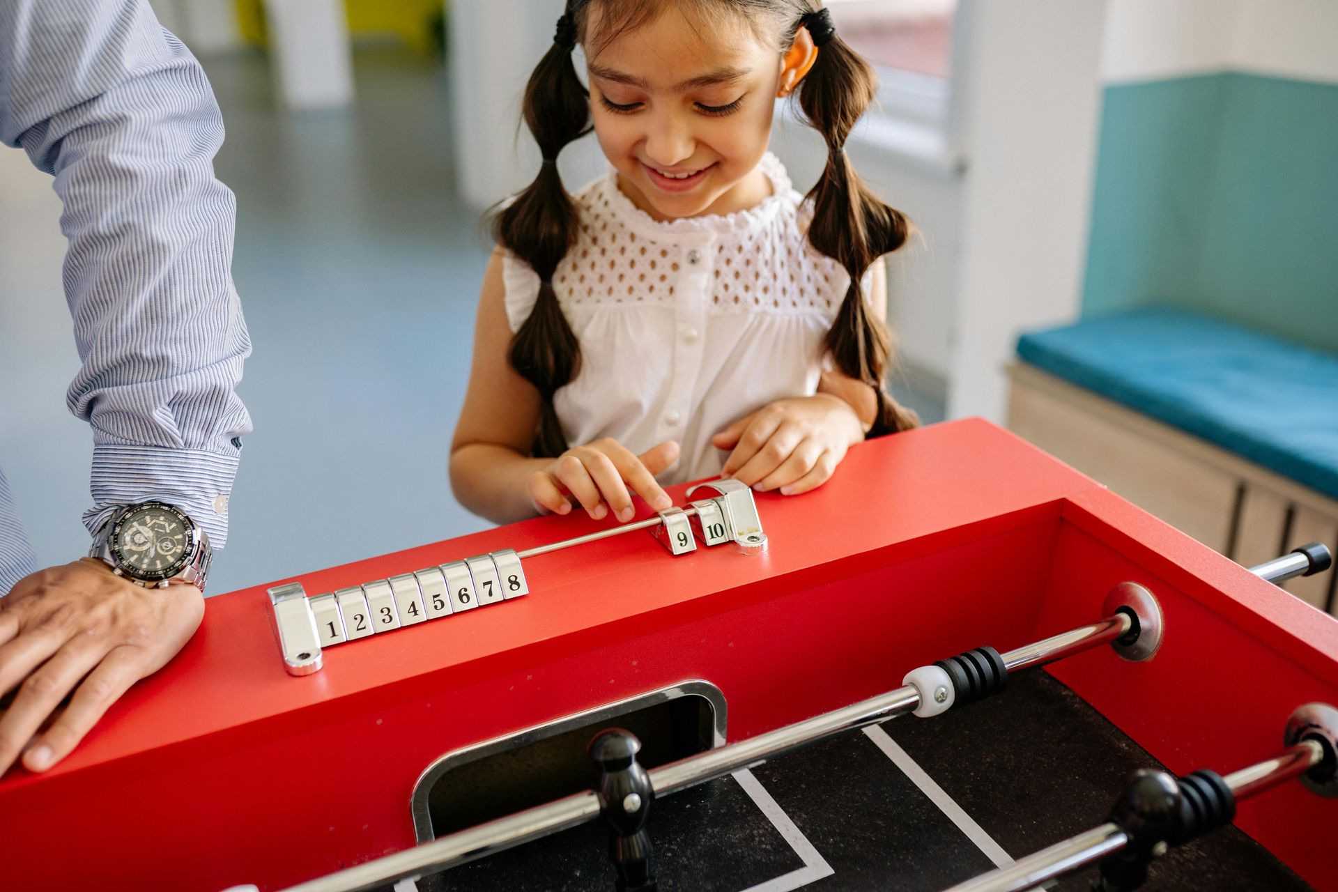 Parents and children in school hallway, greeting teacher. Backpacks, smiles, and waving.
