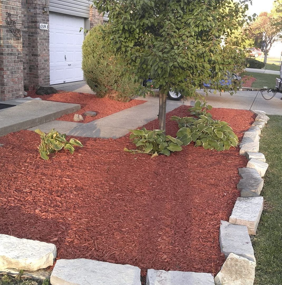 A garden with red mulch and rocks in front of a house.