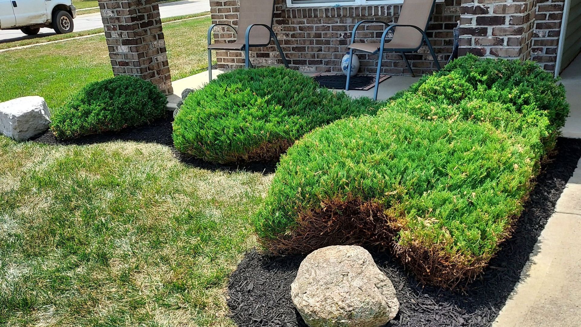 A brick house with a lush green lawn and bushes in front of it.