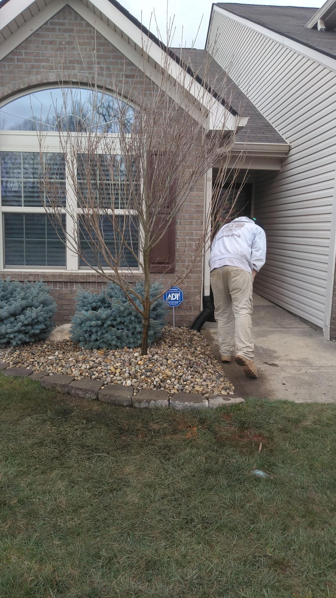 A man in a white jacket is standing in front of a house.