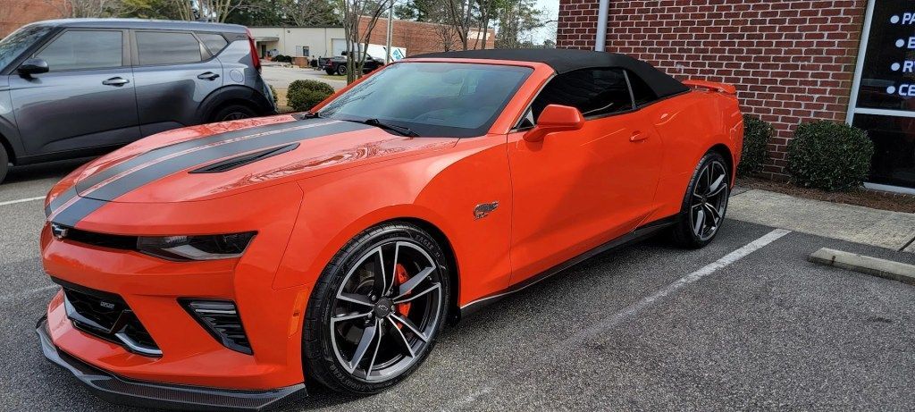 A red convertible chevrolet camaro is parked in a parking lot.