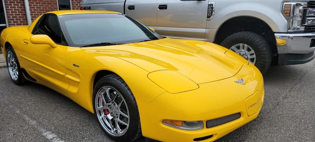 A yellow corvette is parked next to a silver truck in a parking lot.