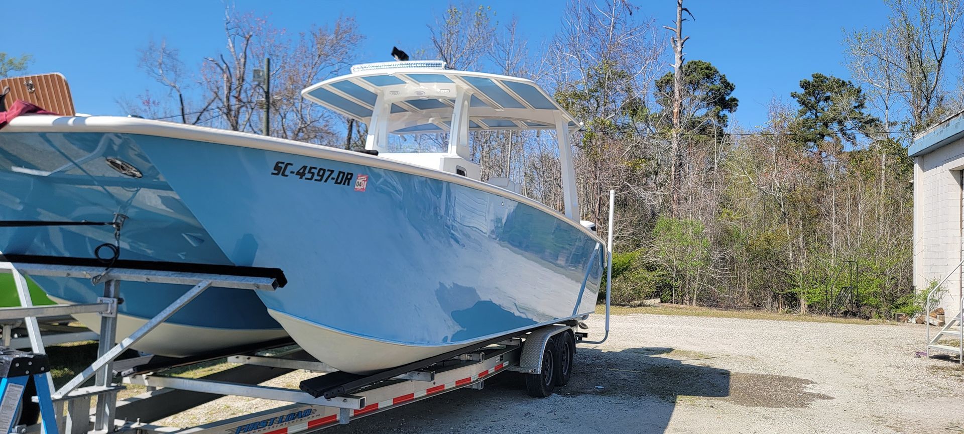 A blue and white boat is on a trailer in a parking lot.